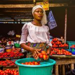 Woman selling fresh tomatoes at an outdoor market stall, showcasing vibrant produce.